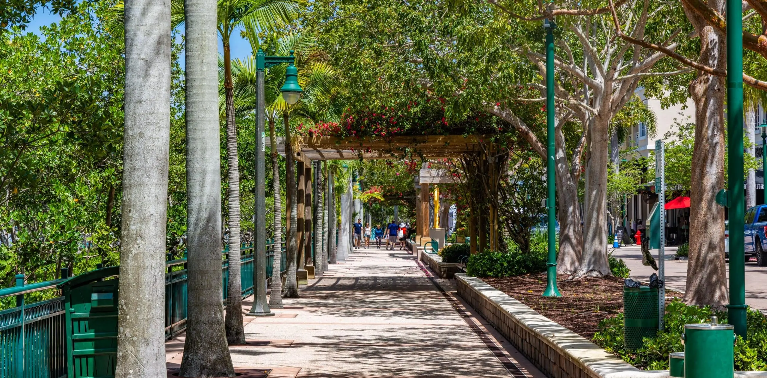 Shaded pedestrian promenade lined with palms and a bougainvillea pergola at Harbourside Place in Jupiter, Florida