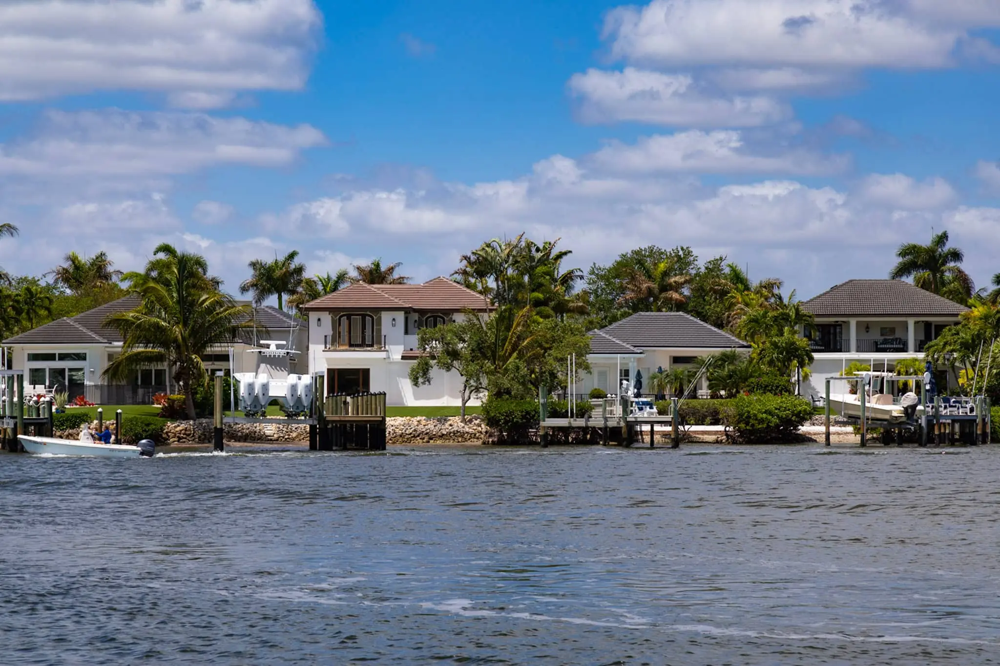 Waterfront homes with private docks and boat lifts, photographed from the water as a small center-console boat runs past