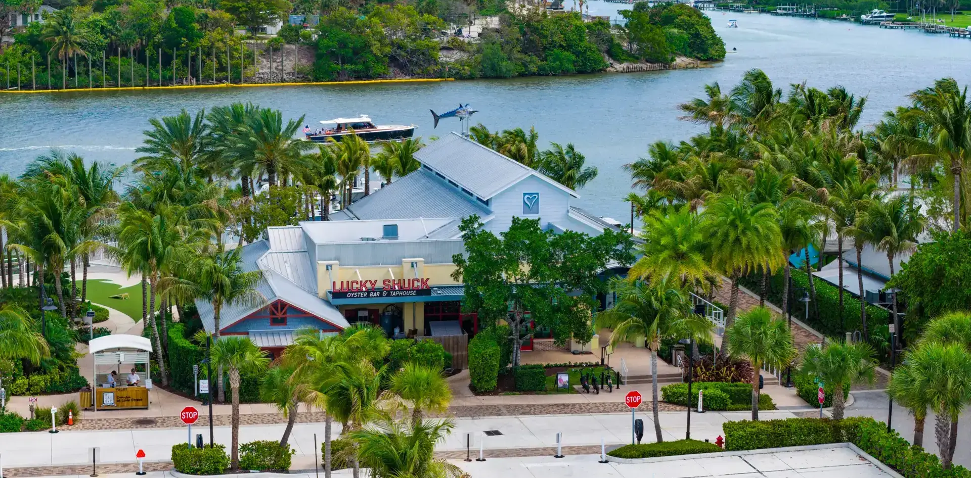 Aerial view of Lucky Shuck Oyster Bar & Taphouse on the Jupiter waterfront, with a boat passing on the Intracoastal behind it