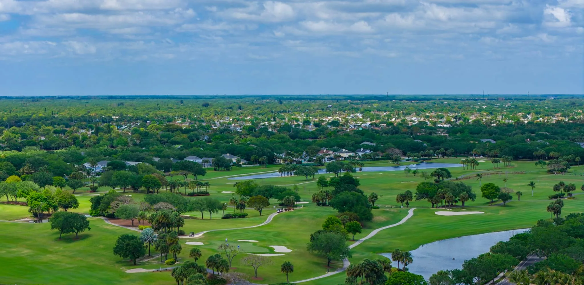 Wide aerial of a golf course, lakes and rooftops stretching to the horizon